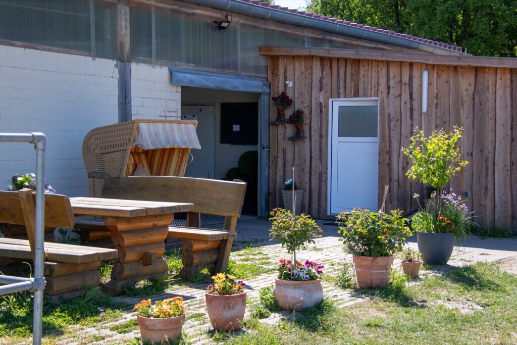 Holzgebäude mit einer Sitzgelegenheit und blühenden Pflanzen in Töpfen im Vordergrund.