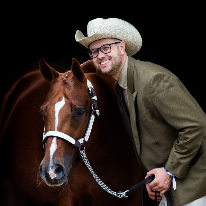 Alexander Eck mit einem braunen Pferd, lächelt in die Kamera, während er einen Cowboyhut trägt.