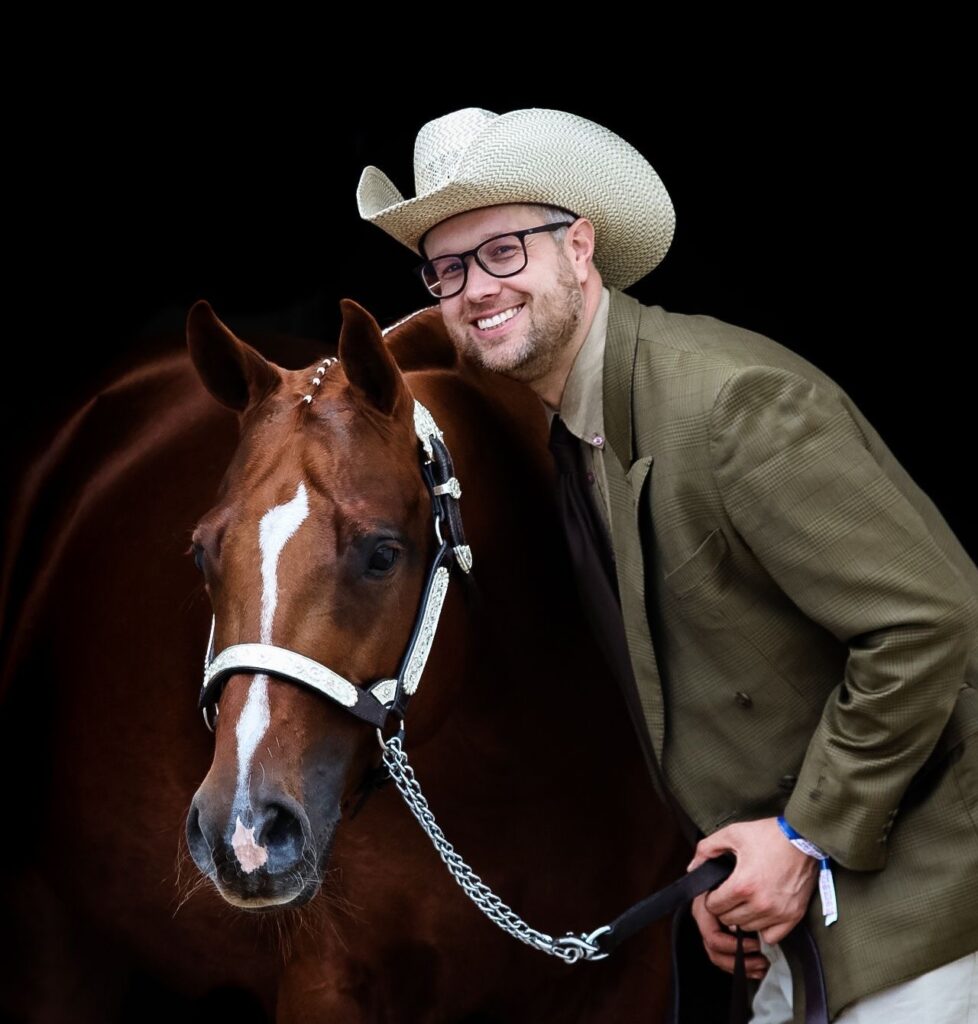 Alexander Eck mit einem braunen Pferd, lächelt in die Kamera, während er einen Cowboyhut trägt.