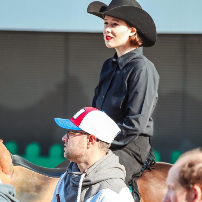 Ricarda Hundt in schwarzer Kleidung und Cowboyhut sitzt auf einem Pferd während einer Veranstaltung.