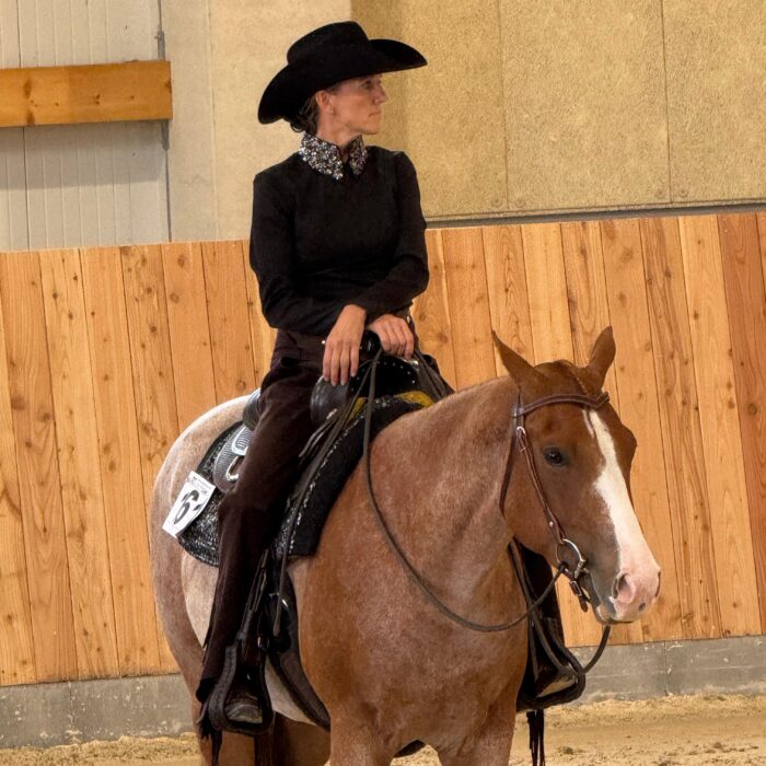 Sandra Thiel reitet auf einem braunen Pferd in einem Reitstall mit Holzverkleidung.